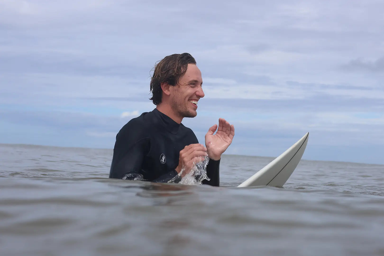 Sam, the founder of Vital Matter, smiling while sitting on his surfboard in the ocean.